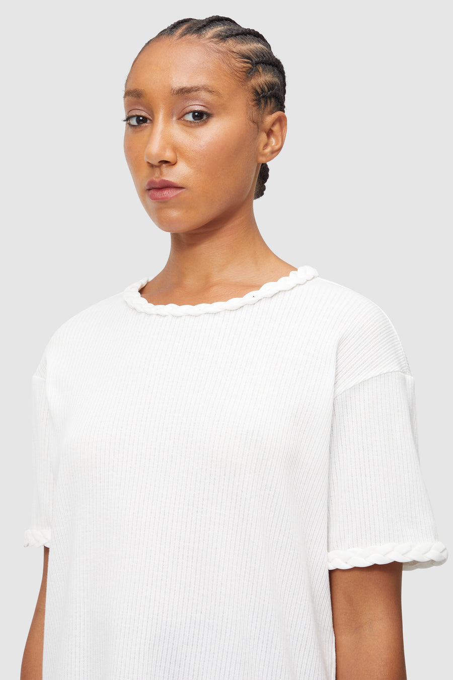 A white ribbed knit top features elegant braided trim accents on the neckline and sleeves, adding subtle sophistication.