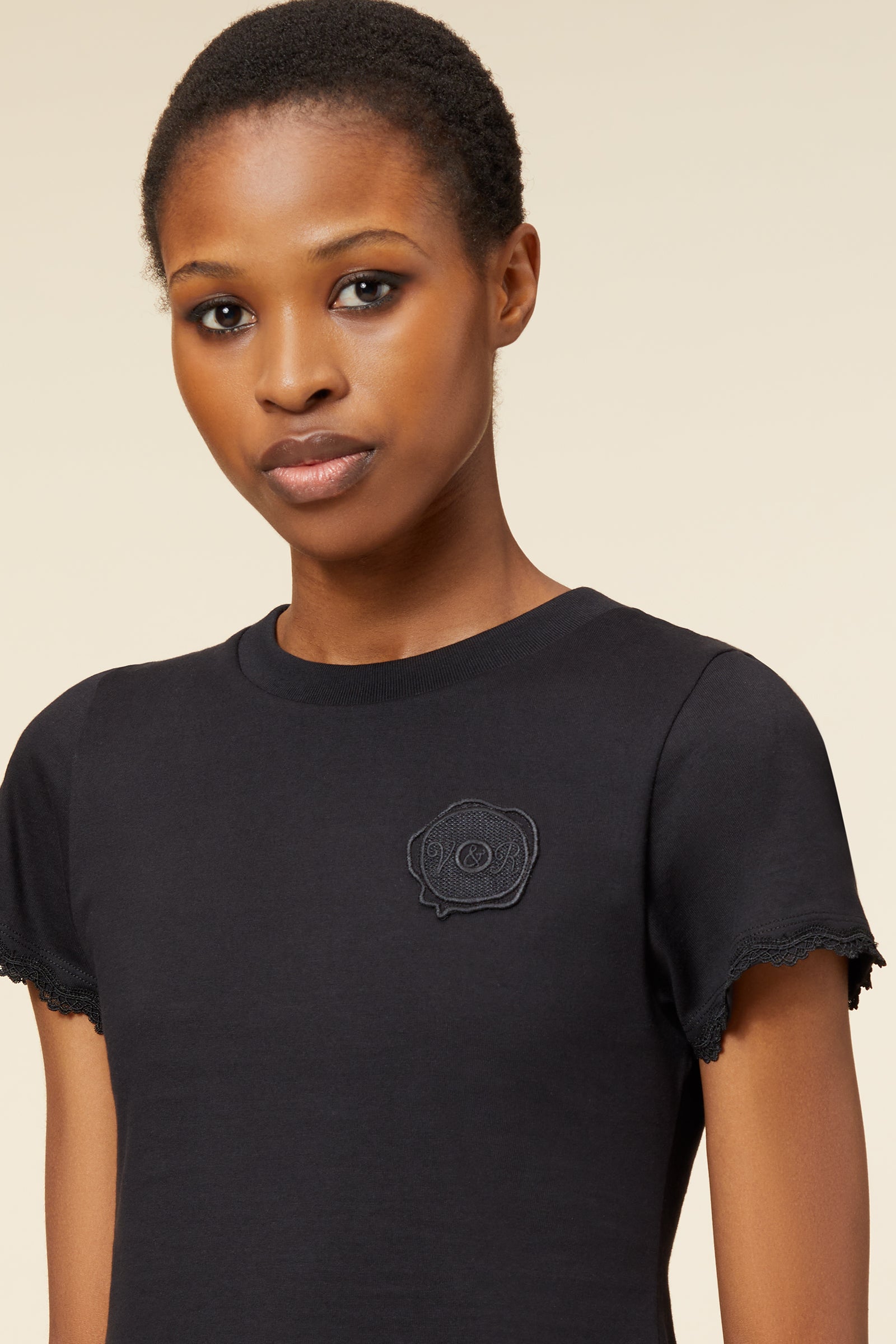 Black cotton T-shirt featuring delicate lace-trimmed sleeves and an embroidered logo patch, offering a minimalist style.