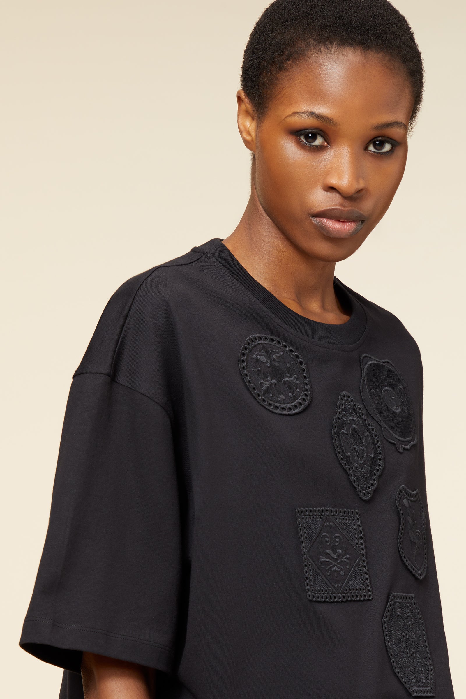 Black oversized T-shirt with intricately embroidered black patches, featuring diverse geometric and floral designs.