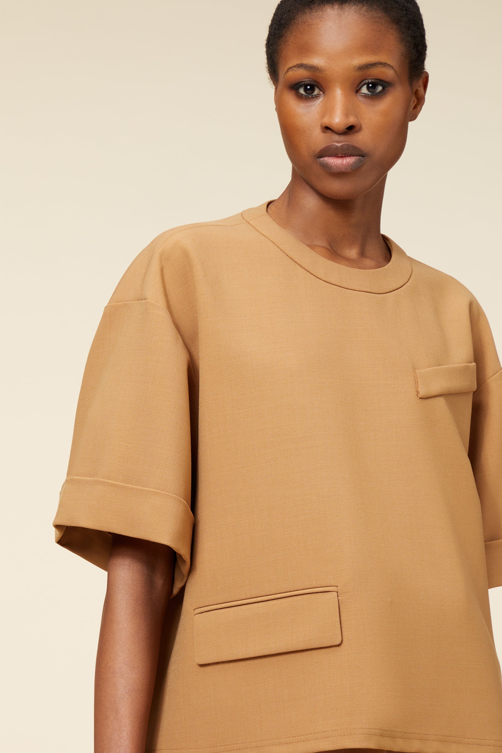 Loose-fit tan cotton top with oversized short sleeves and front patch pocket, featuring clean lines and minimal design.
