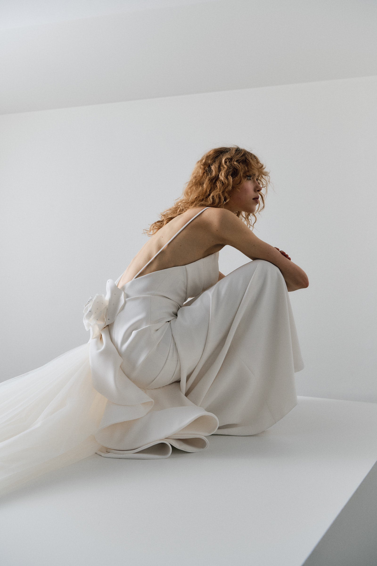 Woman in a white wedding dress standing on a white platform against a plain background