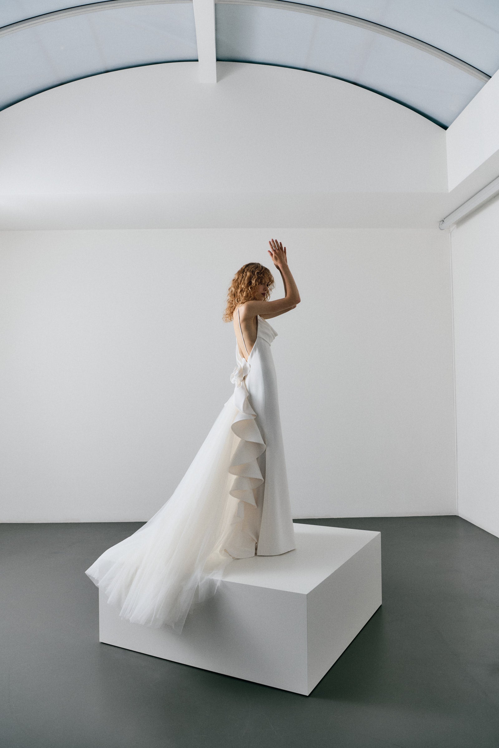 Woman in a white wedding dress standing on a white platform against a plain background