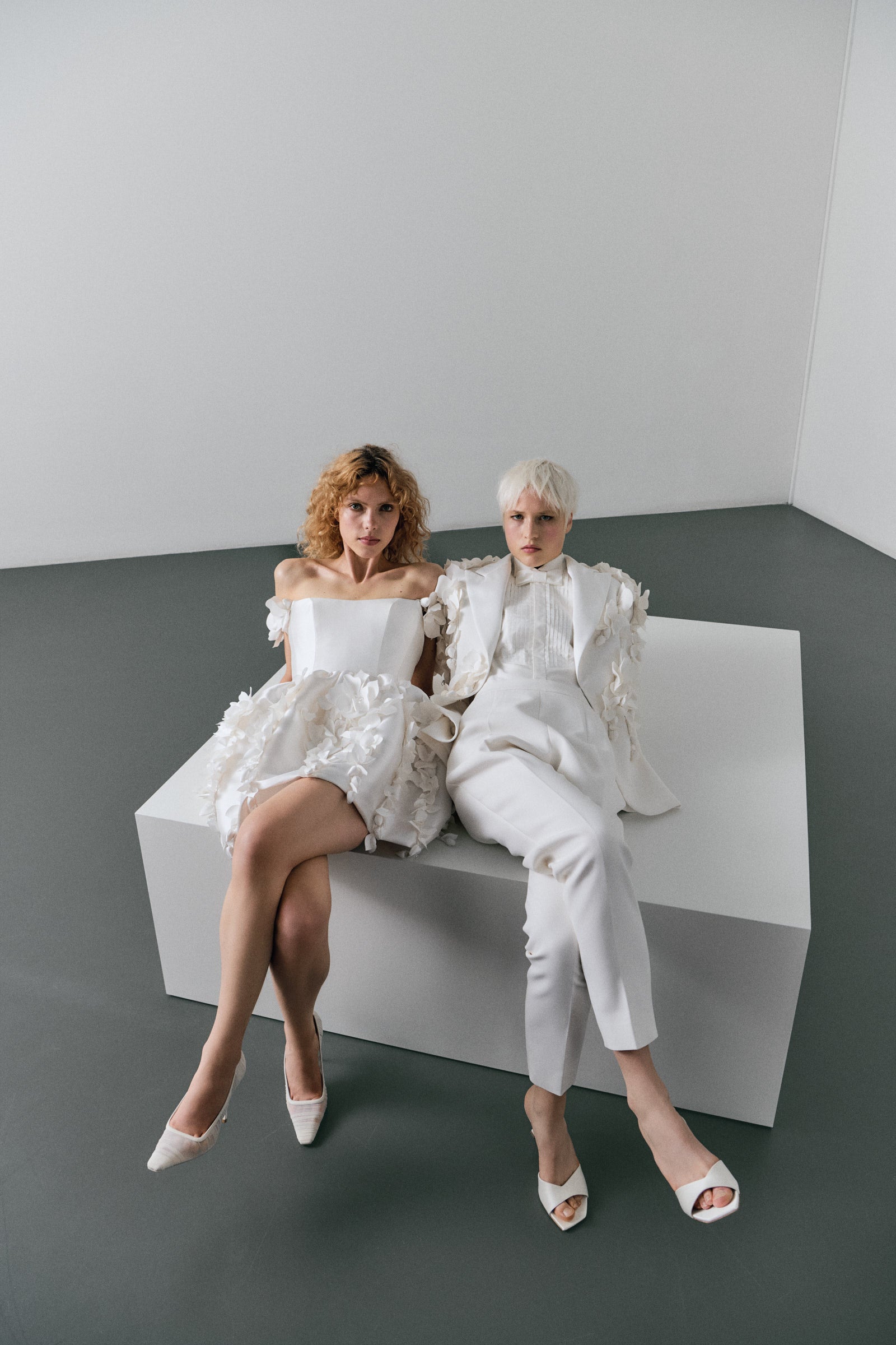 Models wearing a white strapless floral minidress and a white suit against a plain background