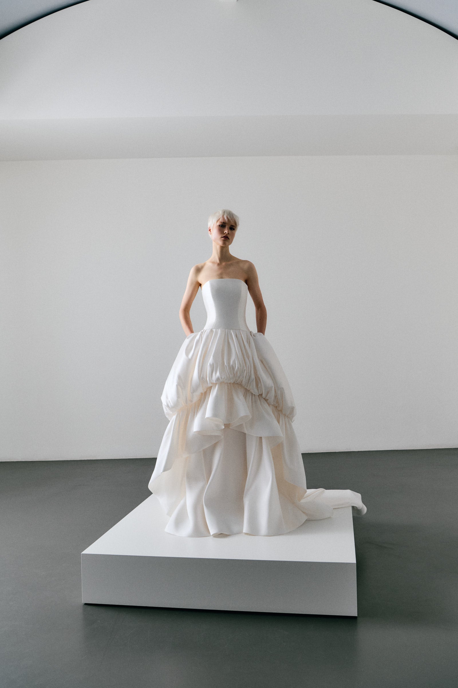 Model wearing a white strapless wedding gown with ruffled bottom on a white background.