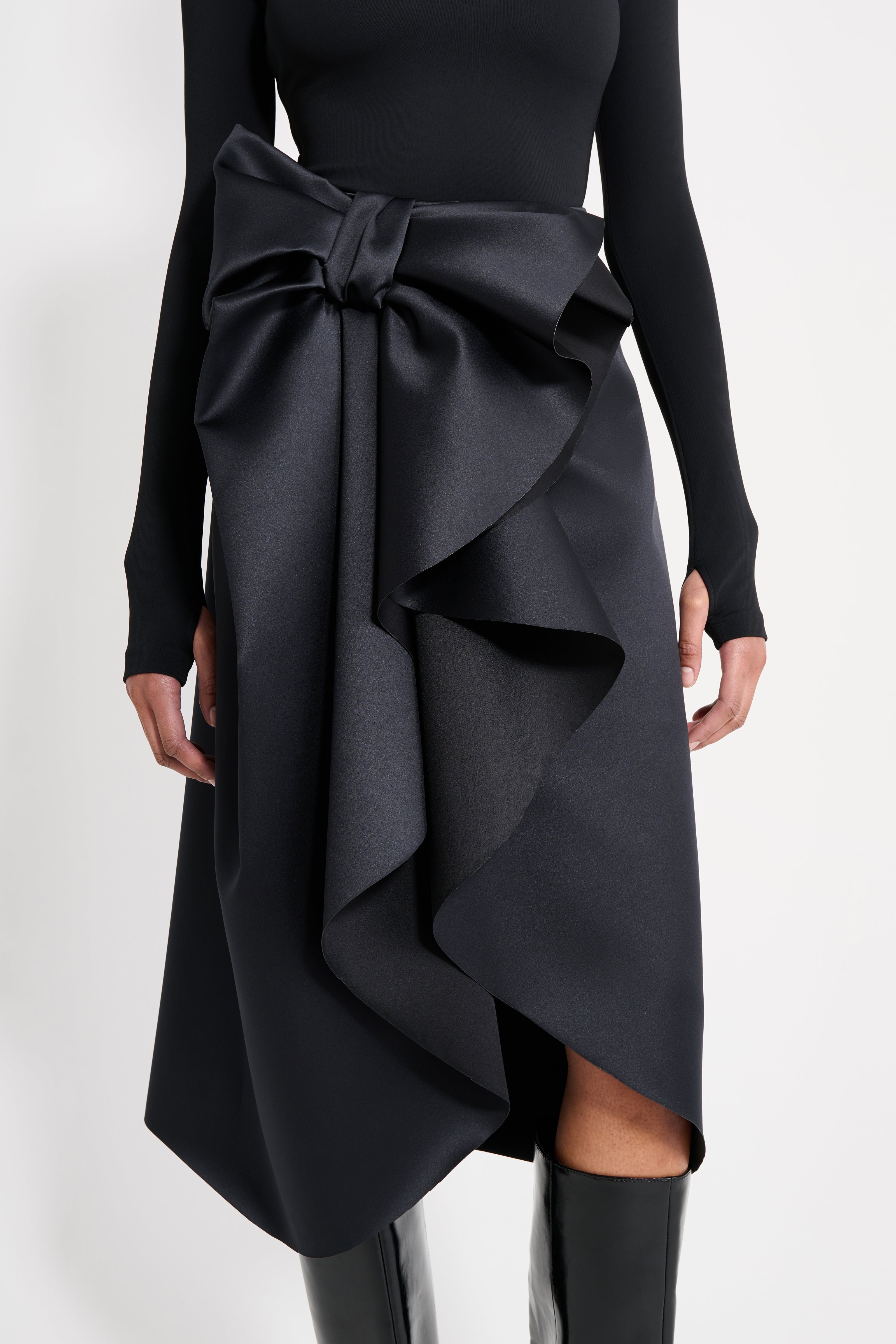 Model wearing a black satin skirt with a black long-sleeve top on a white background.
