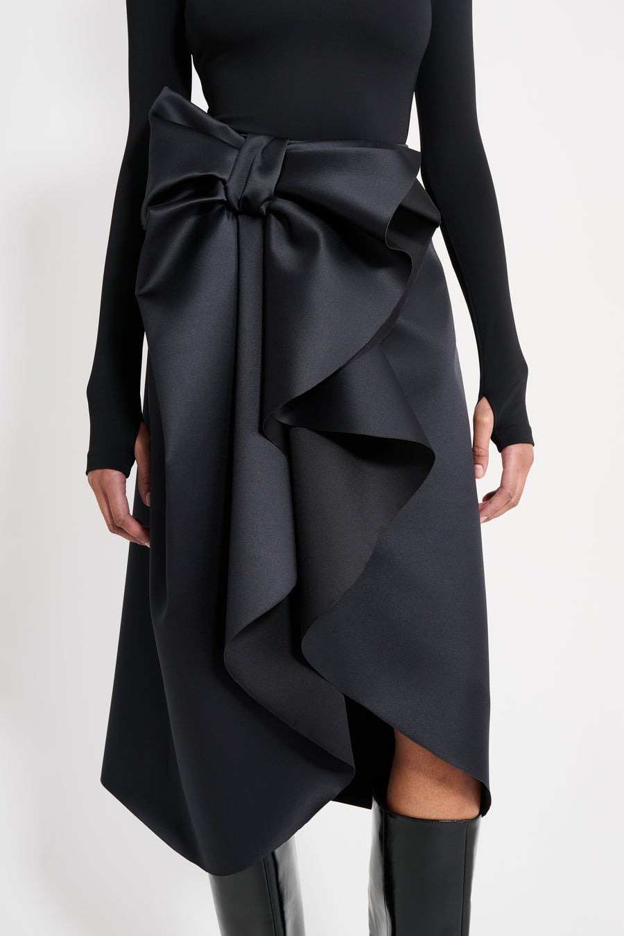 Model wearing a black satin skirt with a black long-sleeve top on a white background.