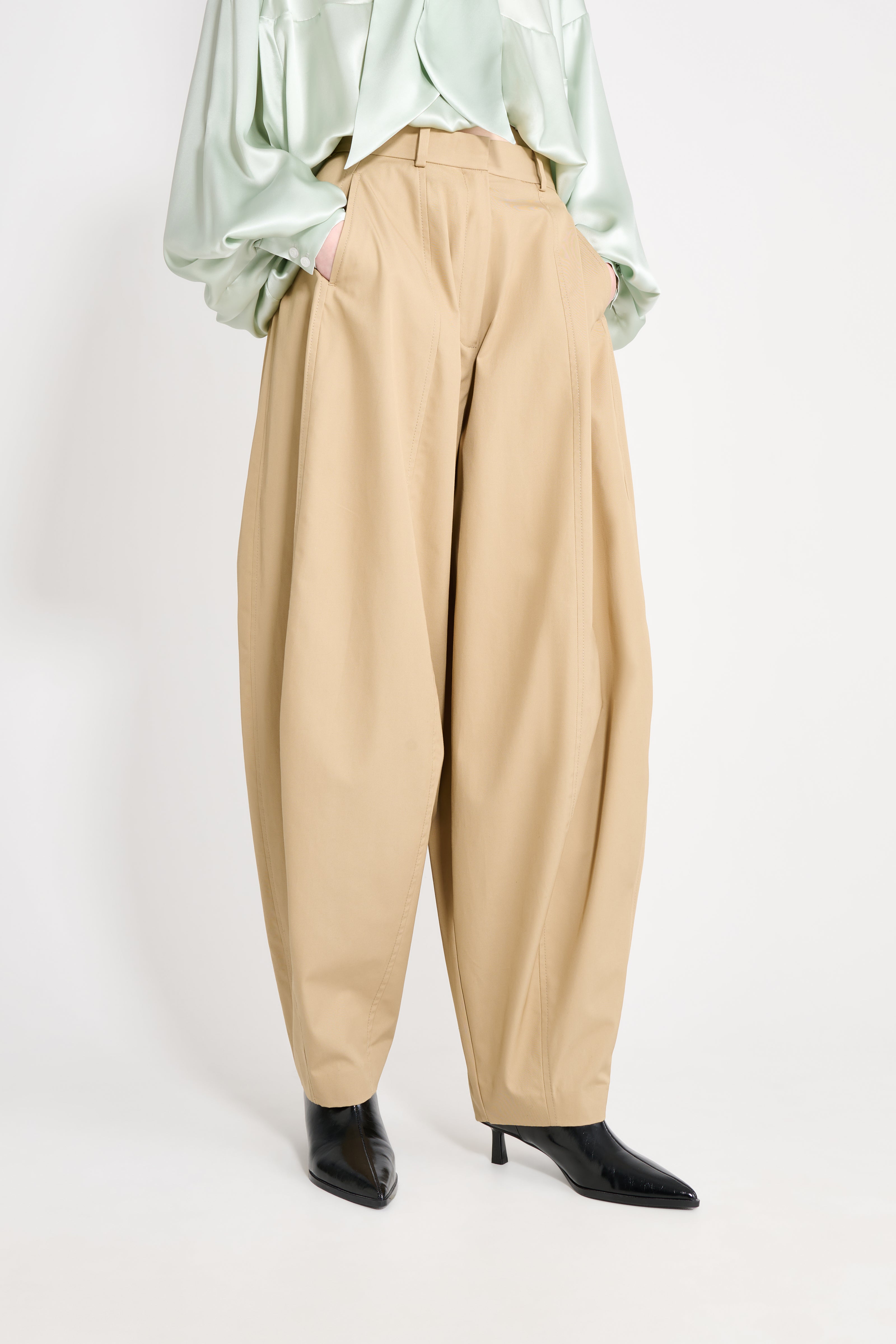 Person wearing beige high-waisted pants and a light green top on a white background