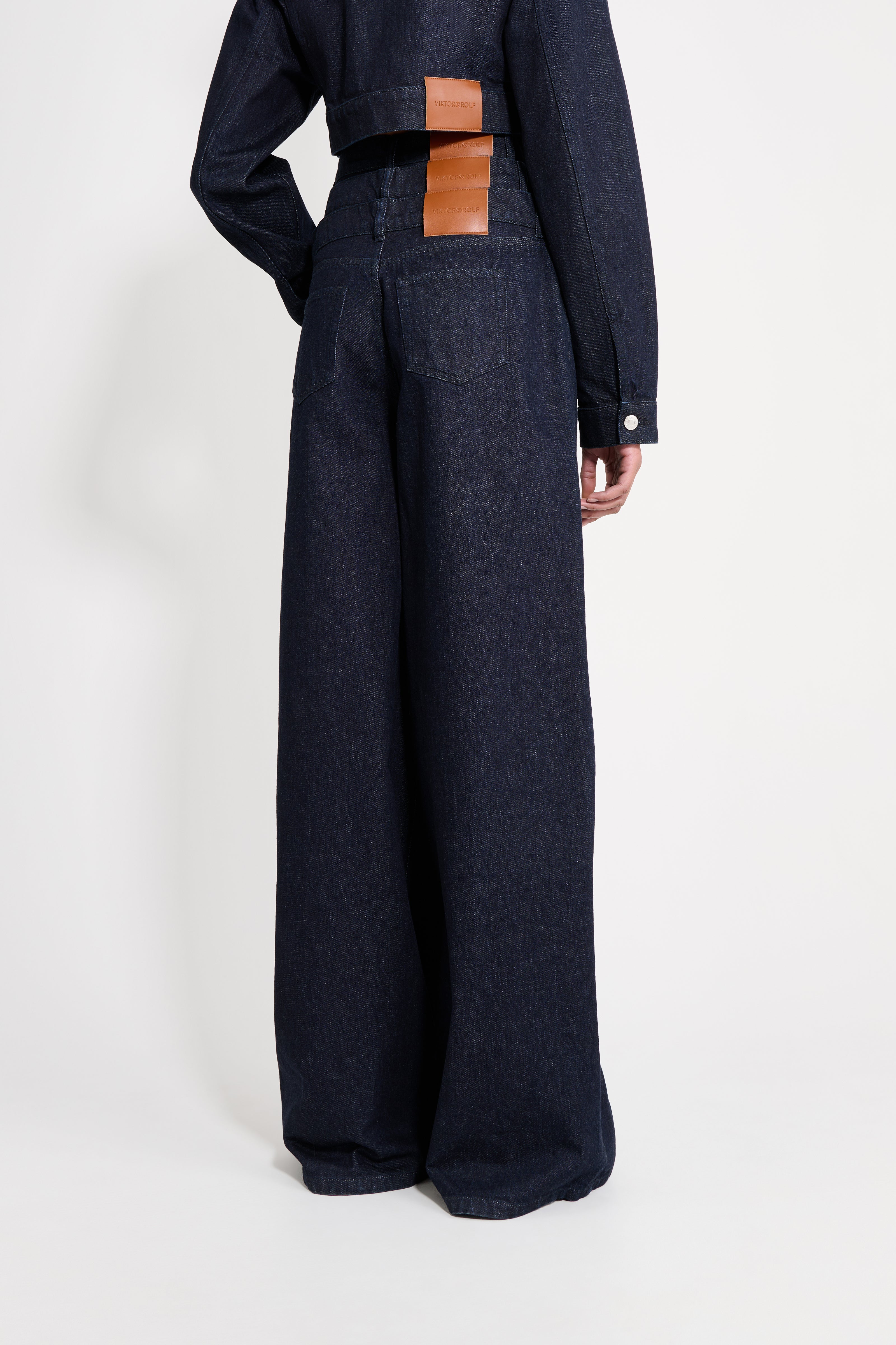 Person wearing dark blue wide-leg pants with a brown leather patch on a white background