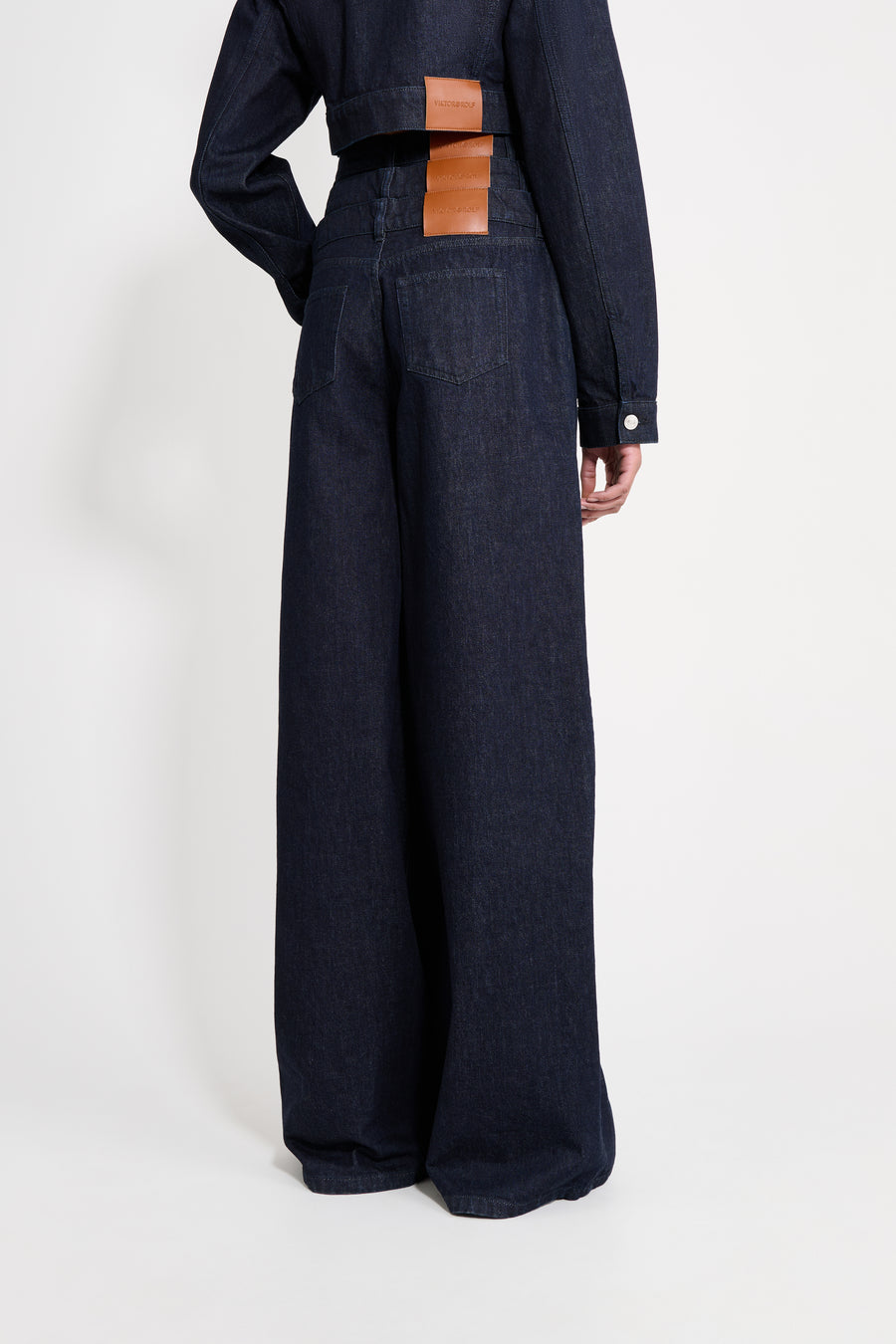 Person wearing dark blue wide-leg pants with a brown leather patch on a white background