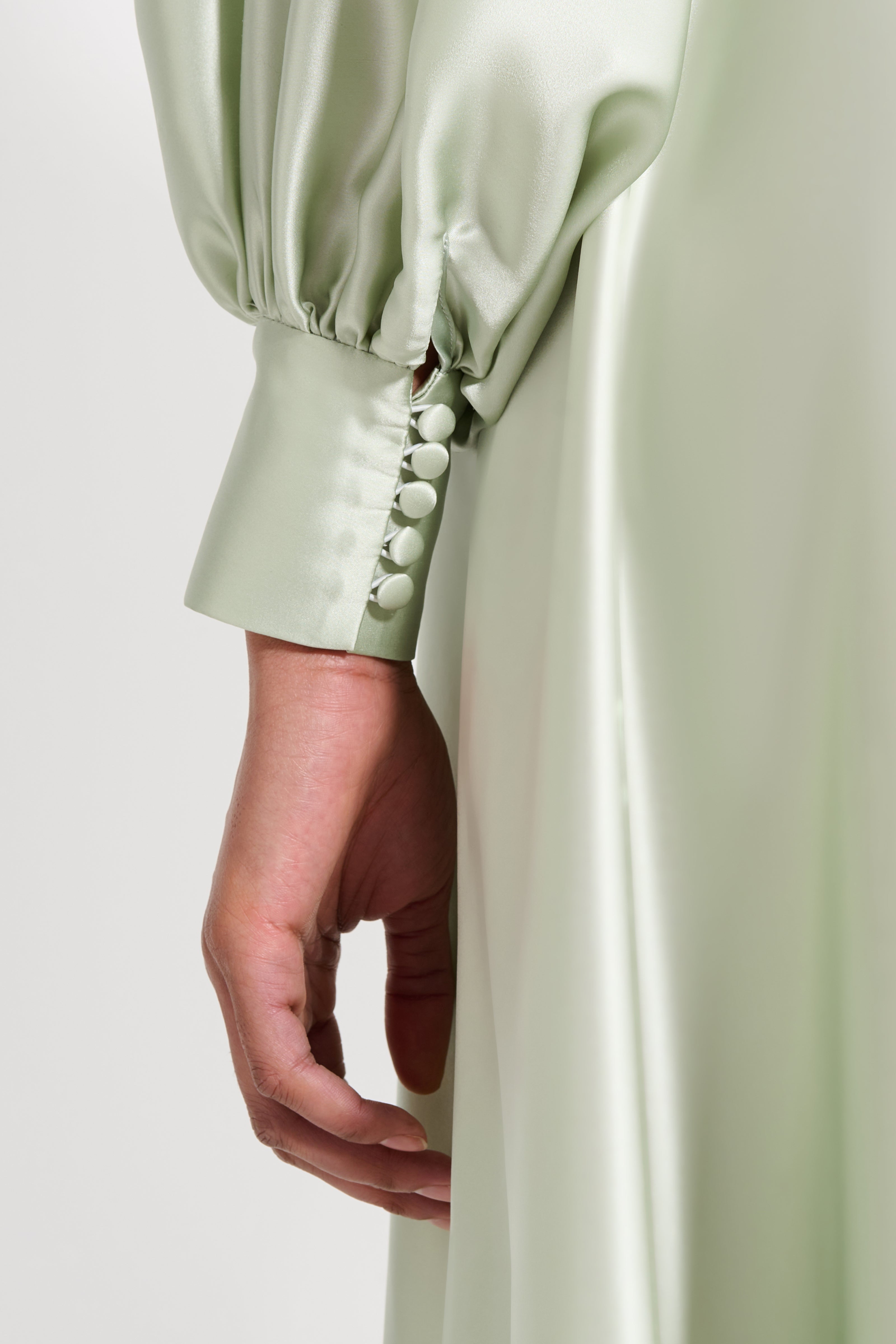 Close-up of a person wearing a light green dress with buttoned cuffs on a plain background