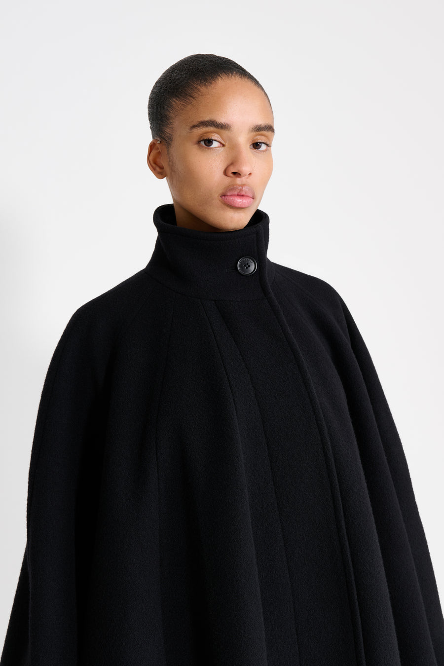 Person wearing a black cape against a white background