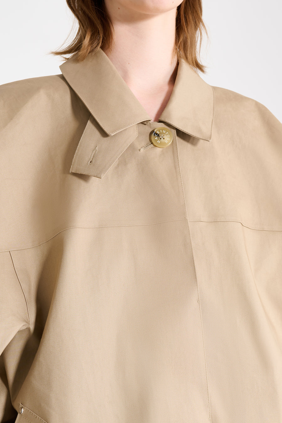 Close-up of a beige coat with a collar and button on a white background