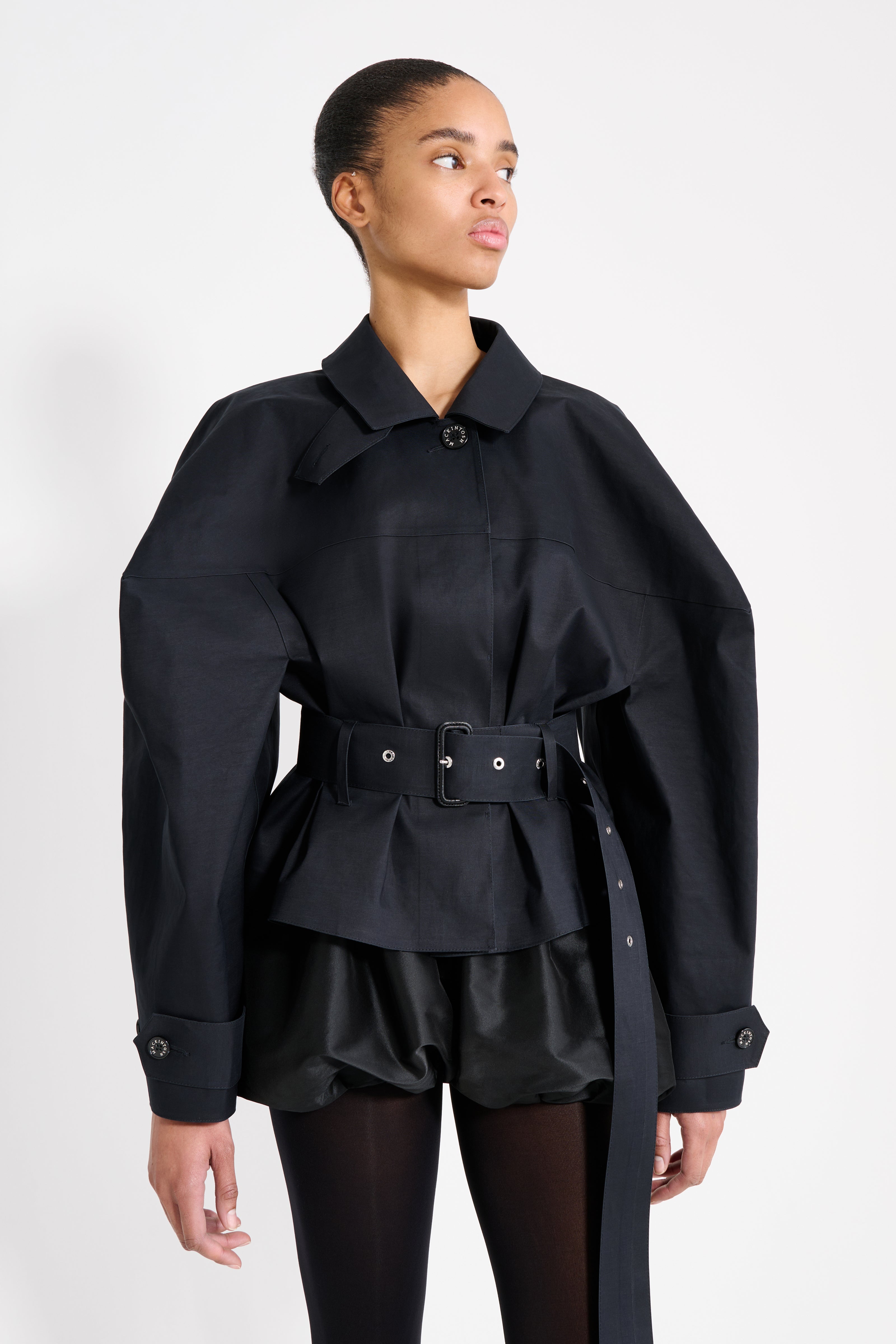 Person wearing a black coat with a belt on a white background
