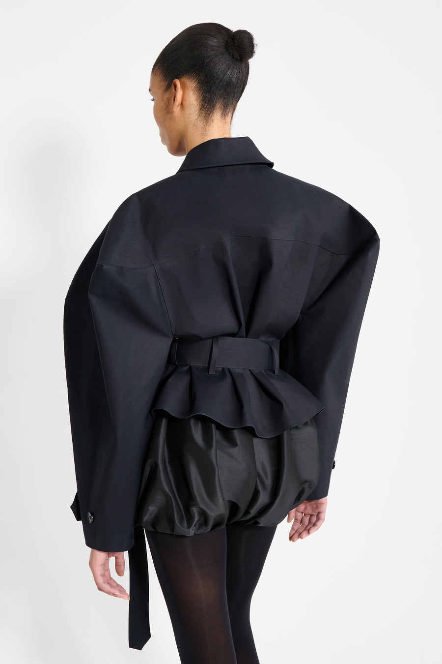 Person wearing a black outfit with ruffled details on a white background