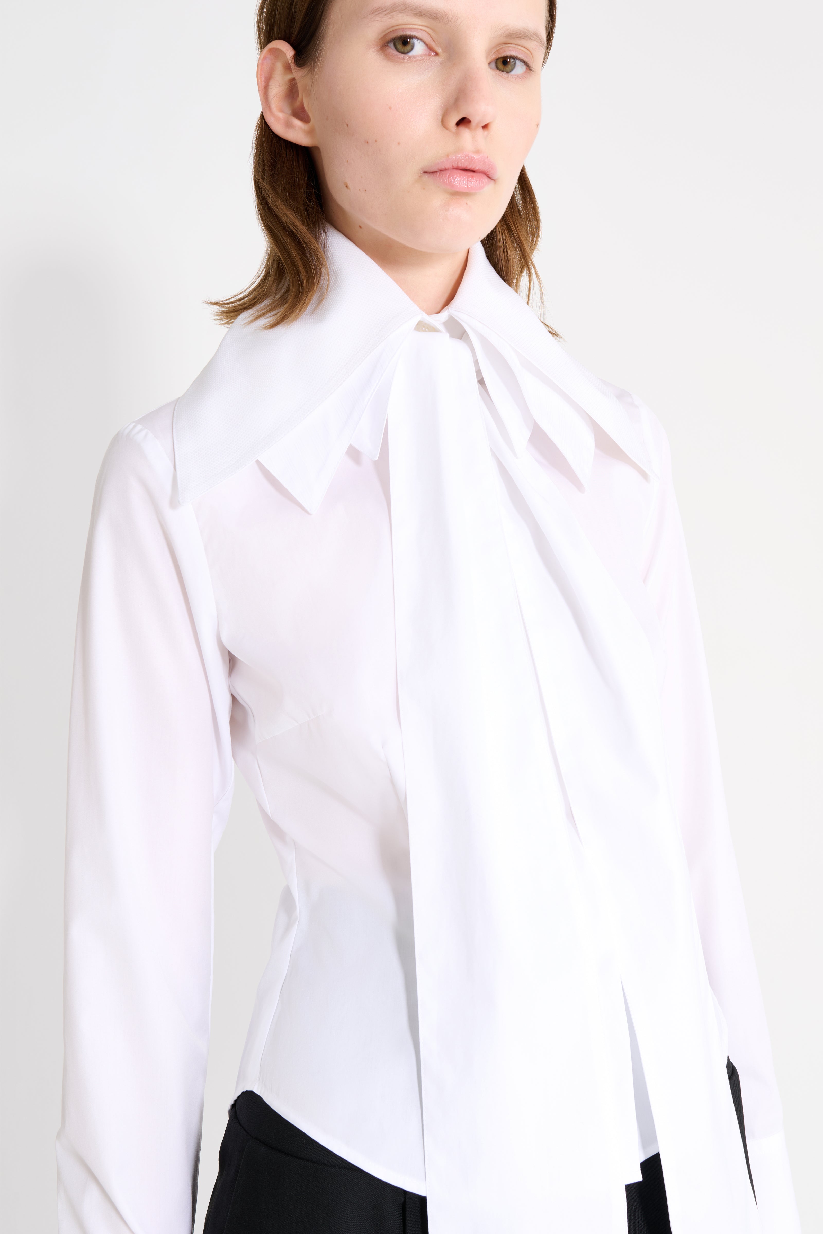 Person wearing a white blouse with a bow tie against a plain background
