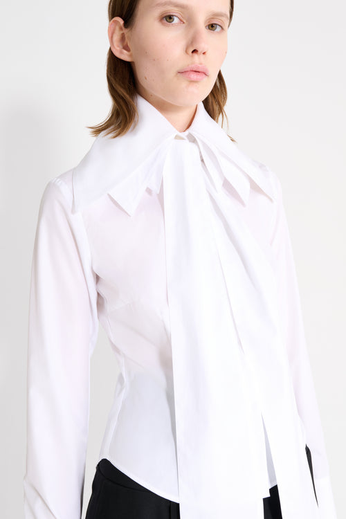 Person wearing a white blouse with a bow tie against a plain background