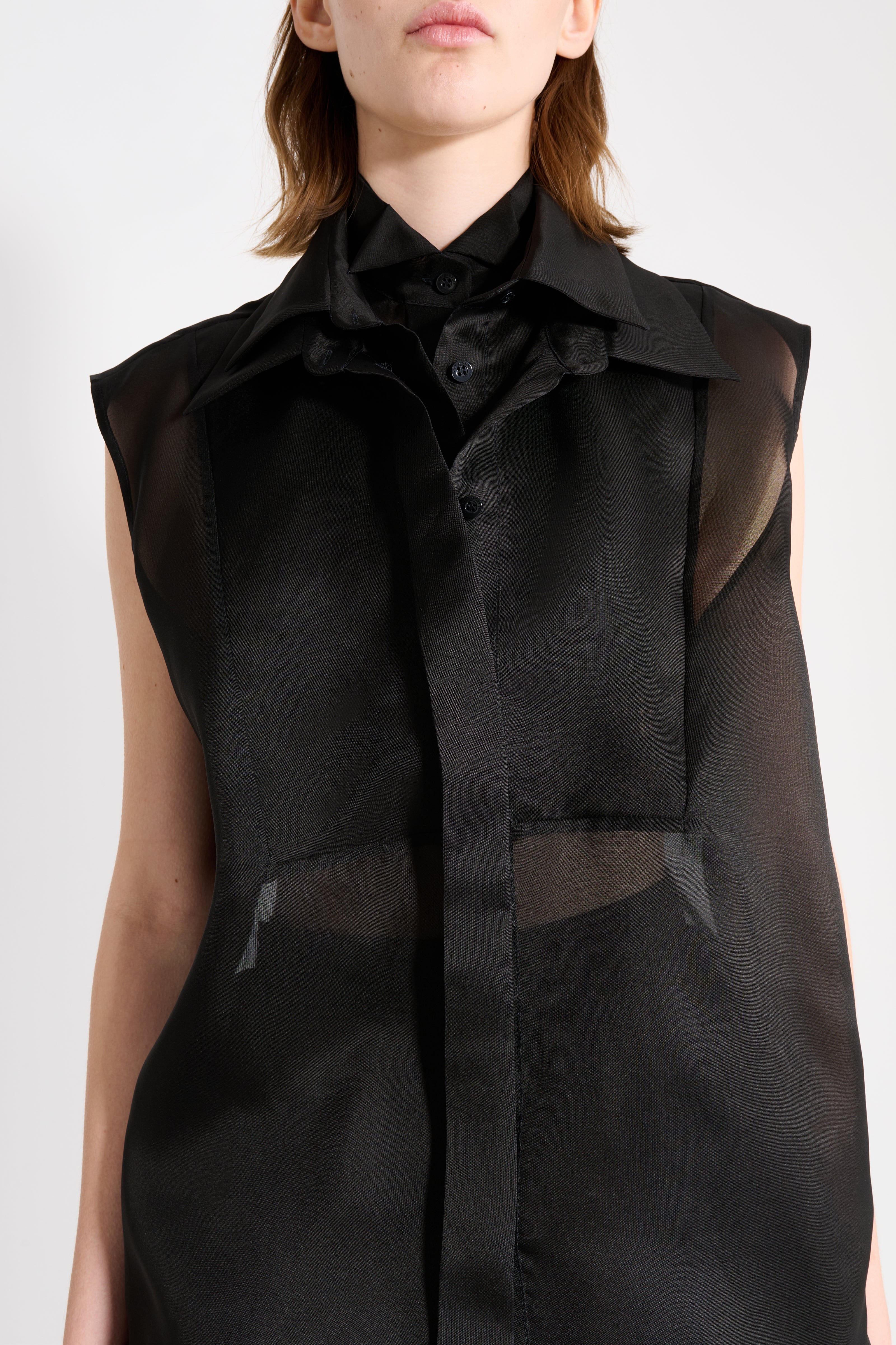 Black sleeveless garment with sheer overlay on a white background