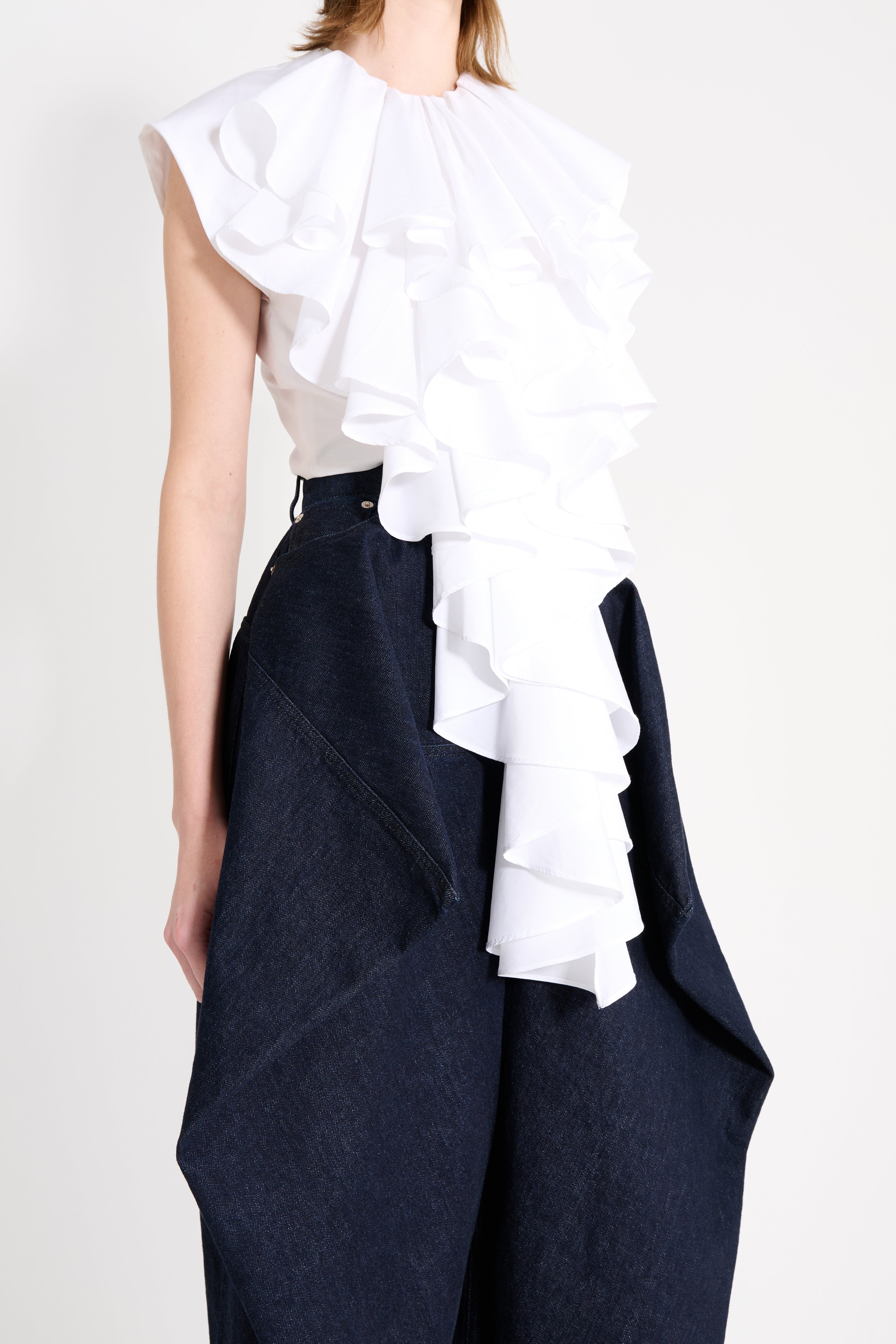 Person wearing a white ruffled top and navy pants on a plain background