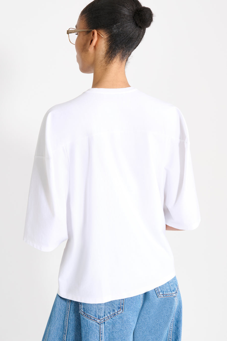 Person wearing a white top and blue jeans on a plain background