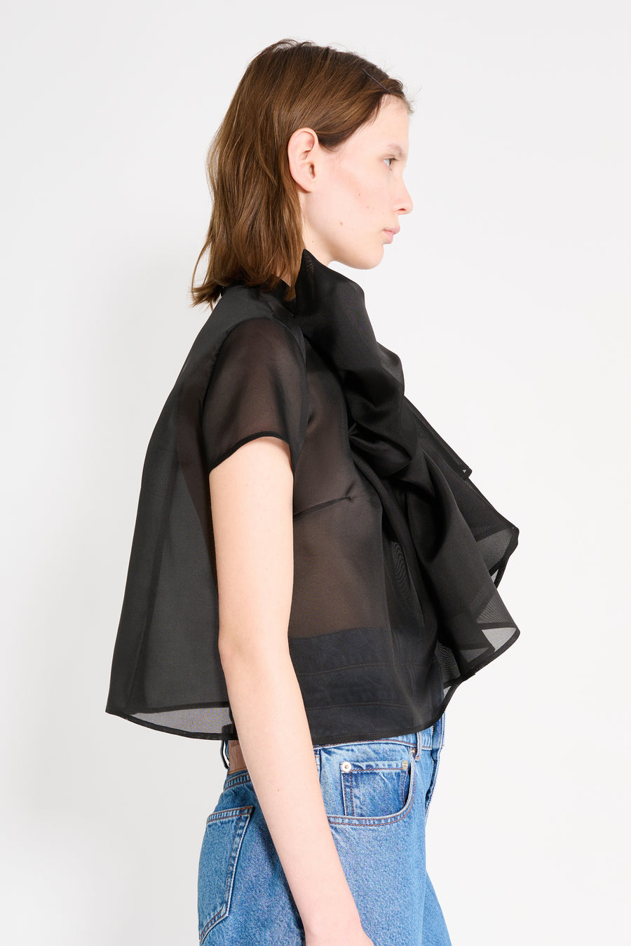 Woman wearing a black sheer top over a dark shirt with blue jeans on a white background