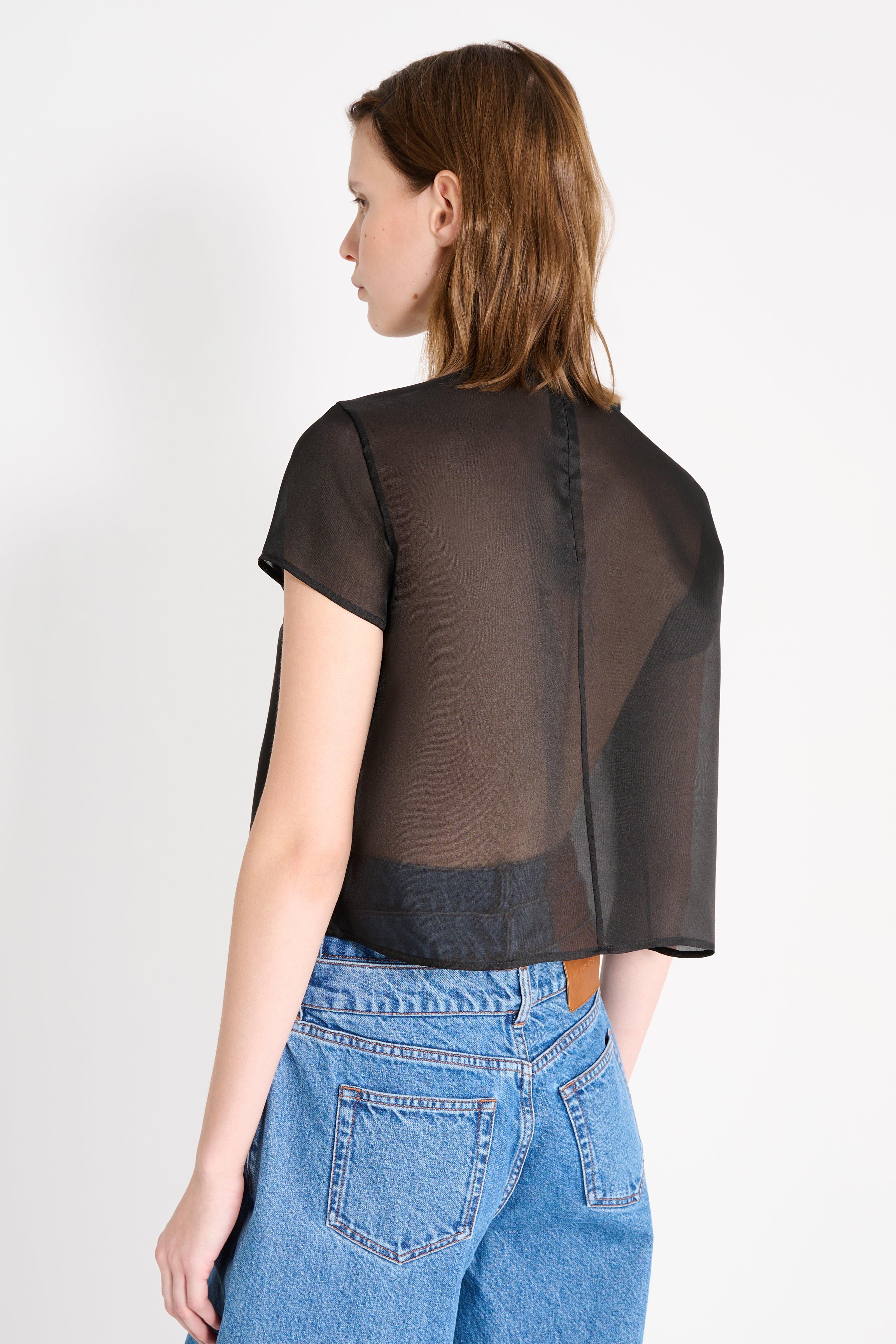 Woman wearing a sheer black top over a denim outfit on a white background