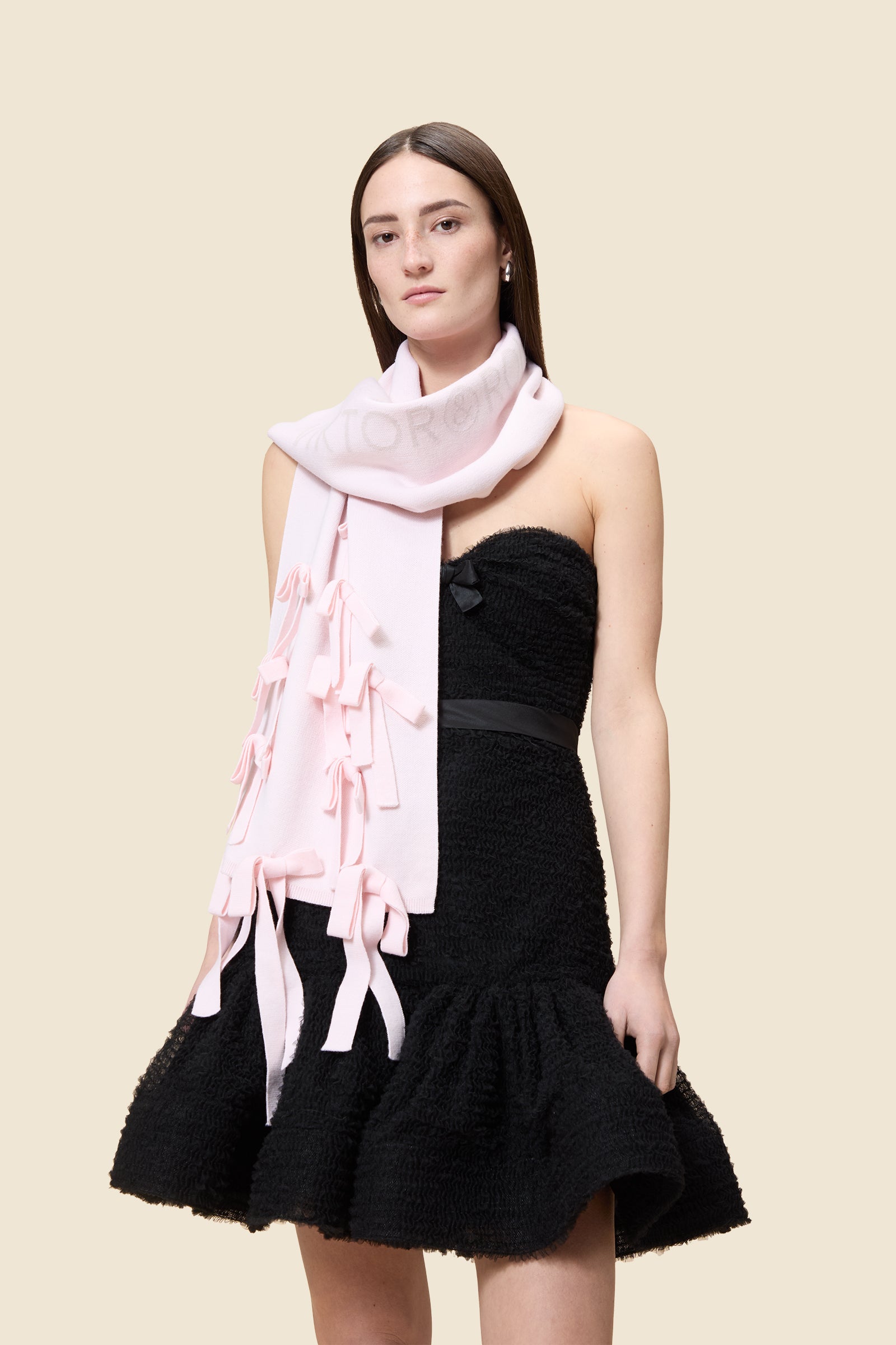 Black textured strapless dress with a ruffle hem, paired with a soft pink scarf embellished with delicate bows.