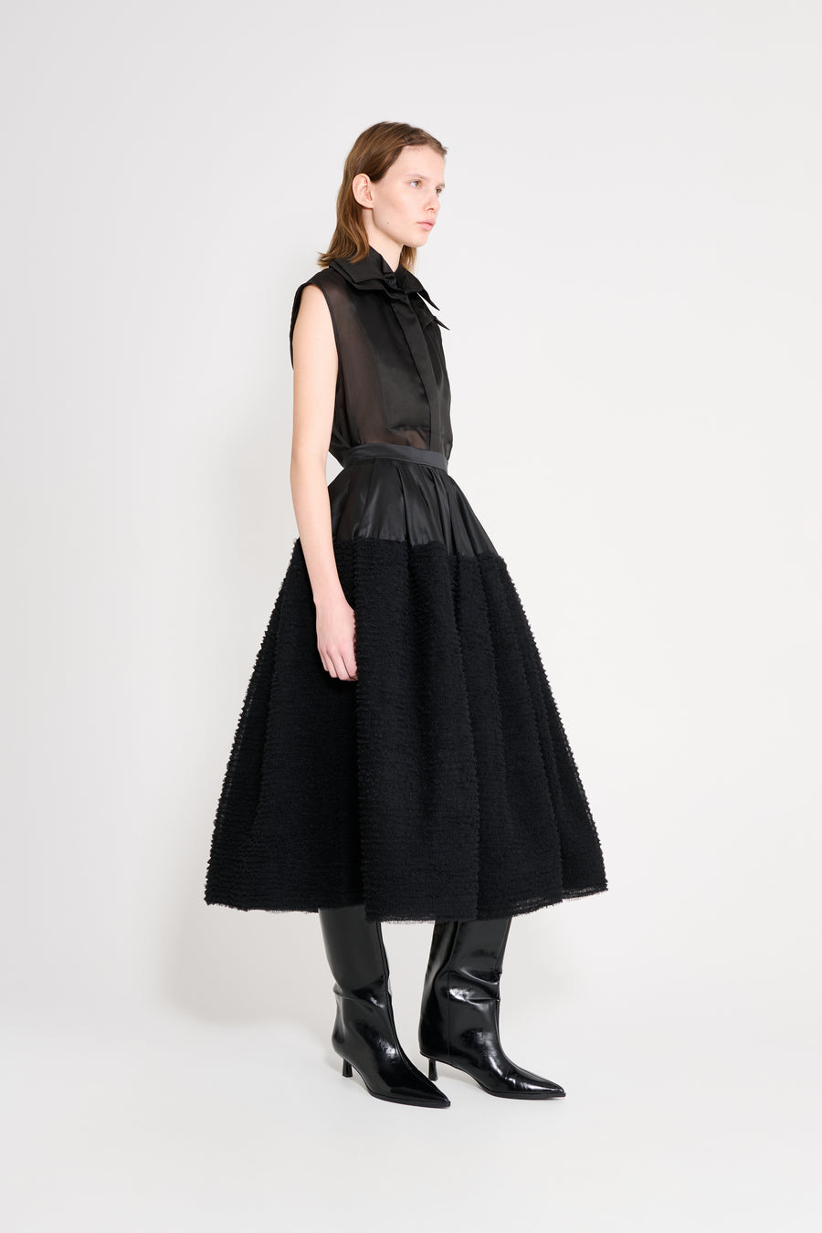 Woman wearing a black sleeveless dress with a fitted bodice and full skirt on a white background