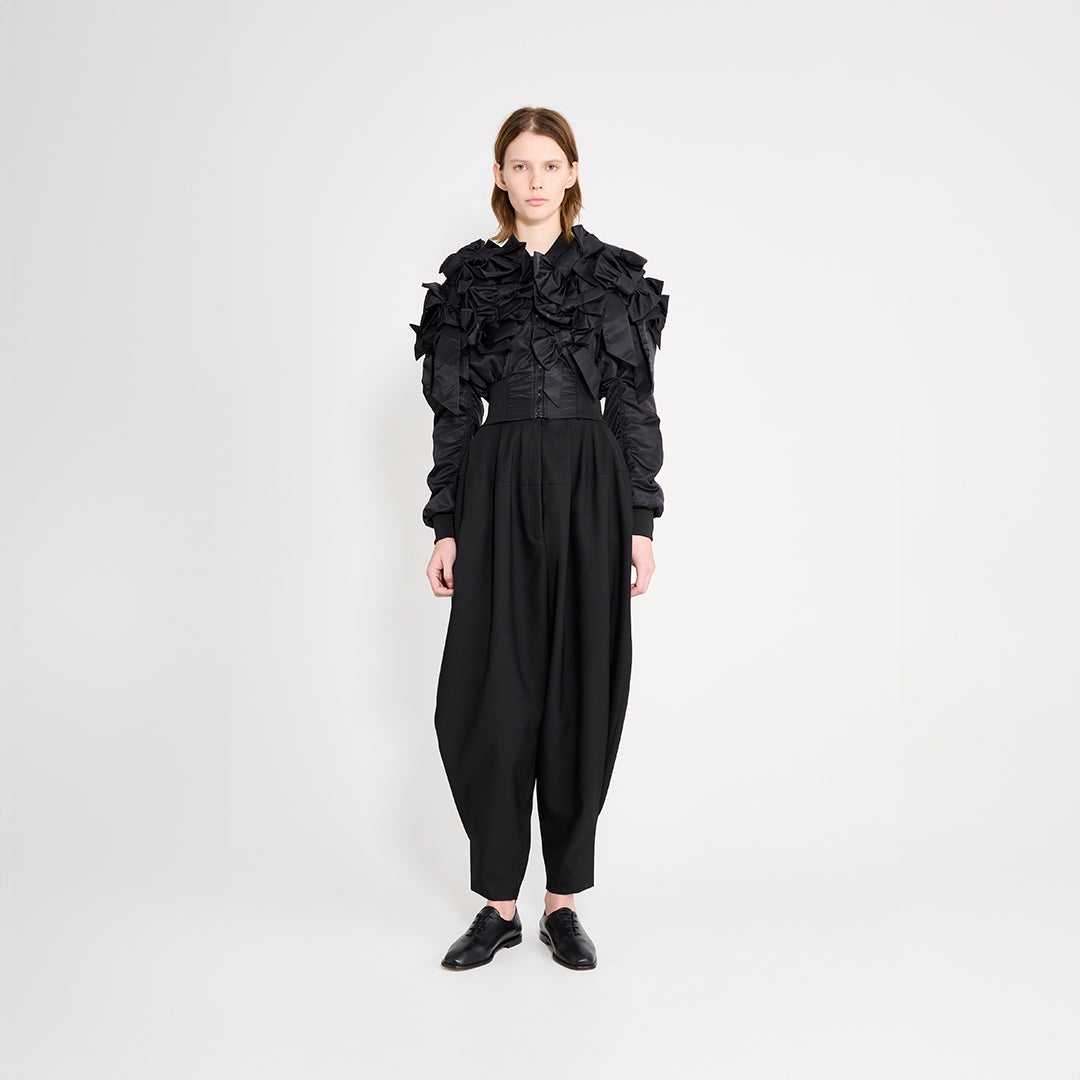 Model wearing black trousers with a bomber jacket on a white trousers.