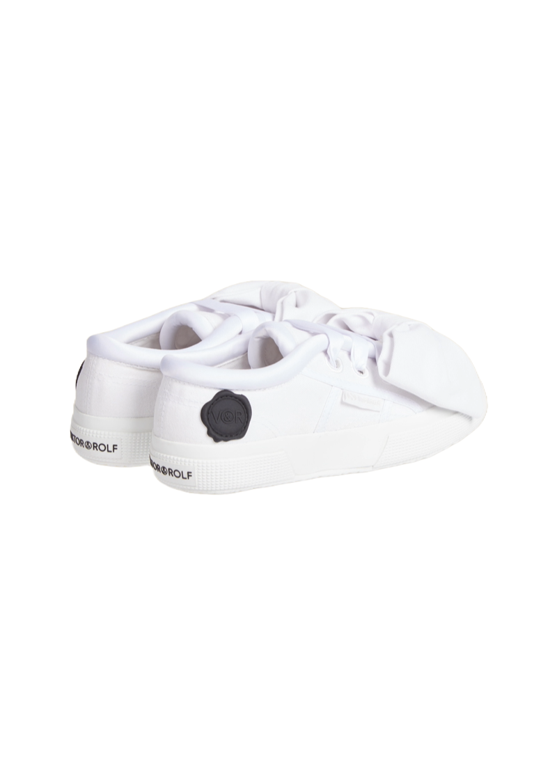 White sneakers featuring soft fabric folds and contrasting black logo detail, combining minimalist design with modern elegance.