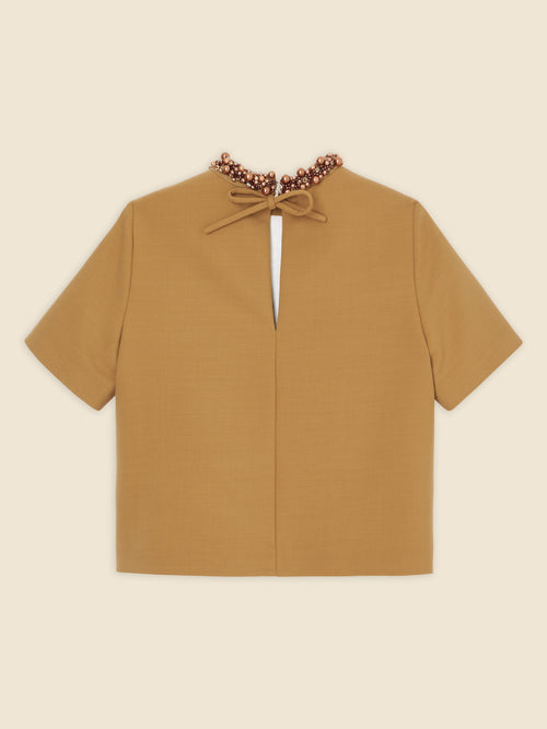 Tan-colored short-sleeve blouse with beaded neckline and back keyhole cutout, featuring a delicate bow tie closure.