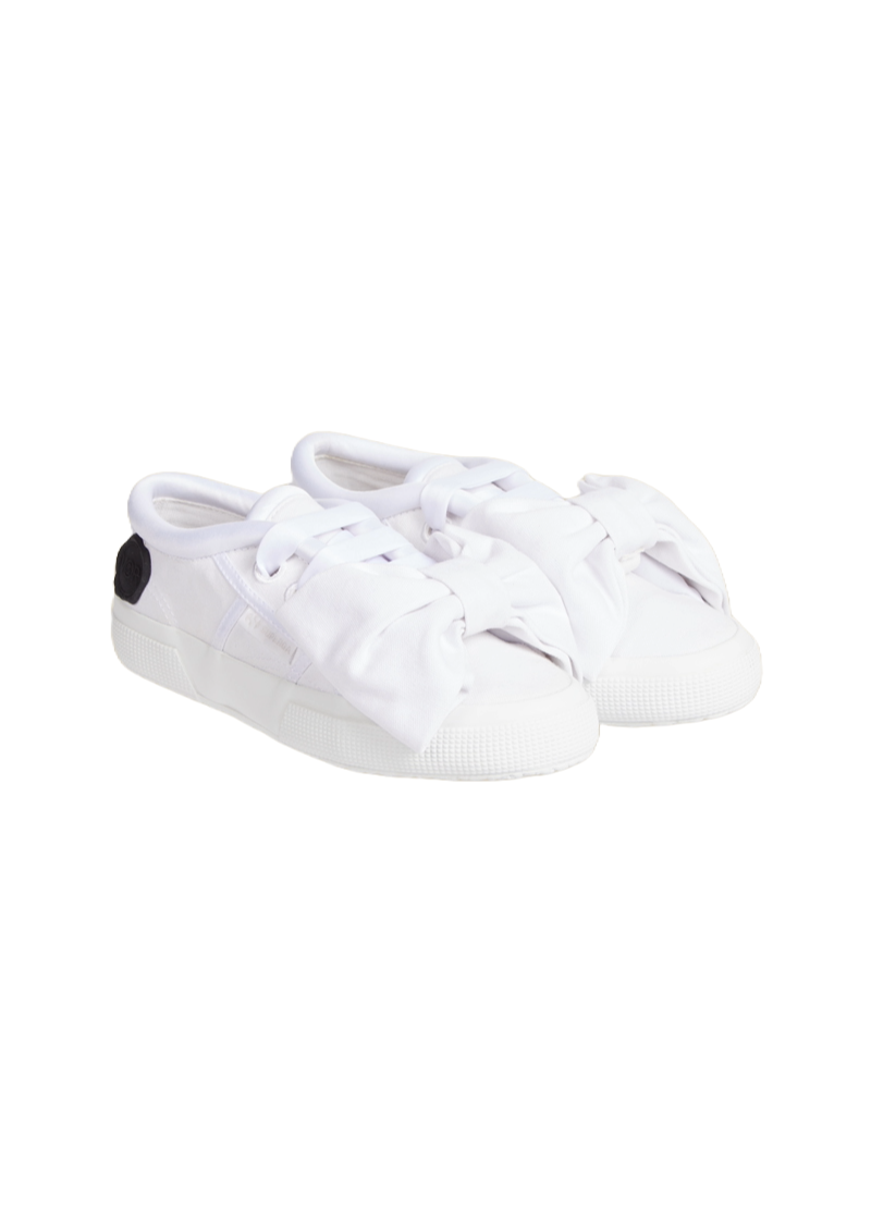 White canvas slip-on sneakers featuring oversized bow details and monochrome accents, blending casual style with elegance.