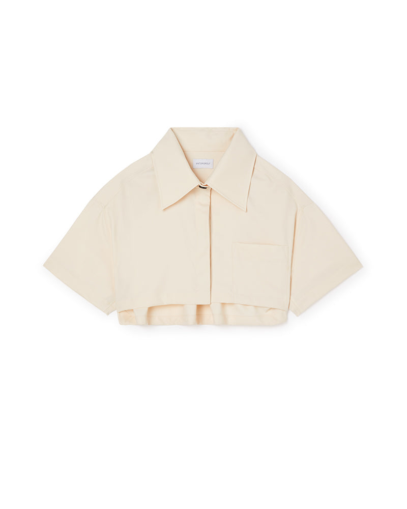 A cropped beige cotton shirt with a sharp collar and short sleeves, featuring a single chest pocket and button closure.