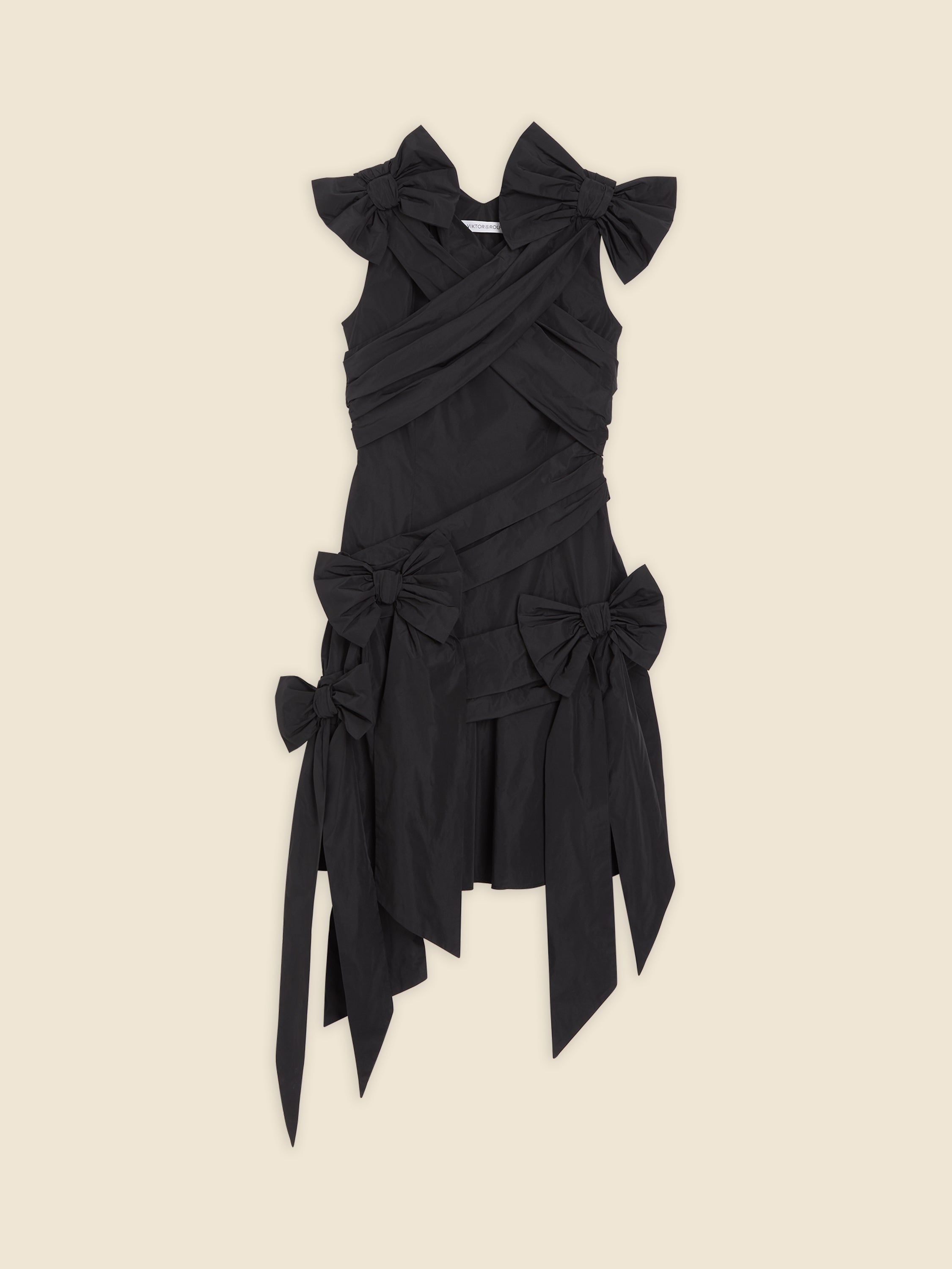 A black sleeveless dress with multiple large bows and an asymmetric hem on a cream background.
