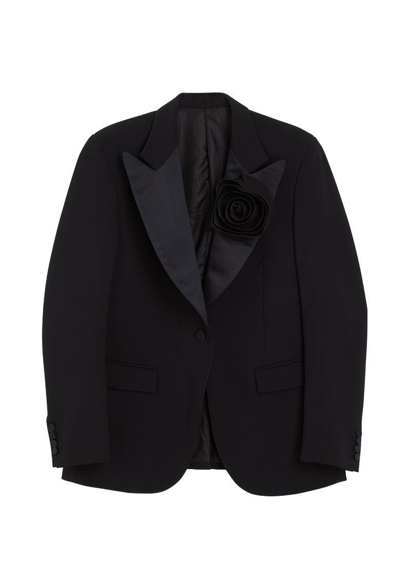 Elegant black tuxedo jacket with satin lapels, single button closure, and a striking fabric rosette on the left chest.