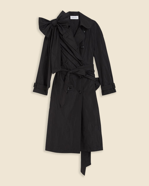 Black trench coat with oversized bow detailing on the shoulder and double-breasted button design, featuring a classic waist belt.