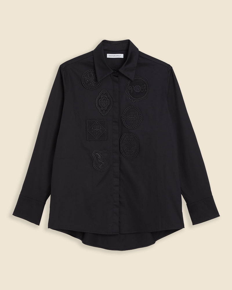 Black shirt with intricate embroidered patches, featuring a classic collar and button-down front, offering a modern and stylish design.