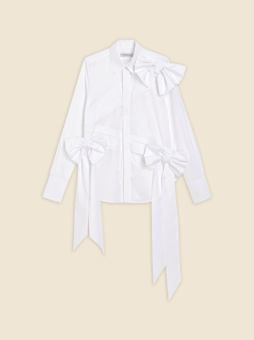 White long-sleeve shirt with decorative bows, featuring buttoned front and classic collar on beige background.