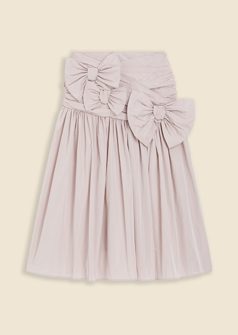 Pale pink knee-length skirt with large decorative bows and gathered waist detailing, offering a feminine and elegant look.
