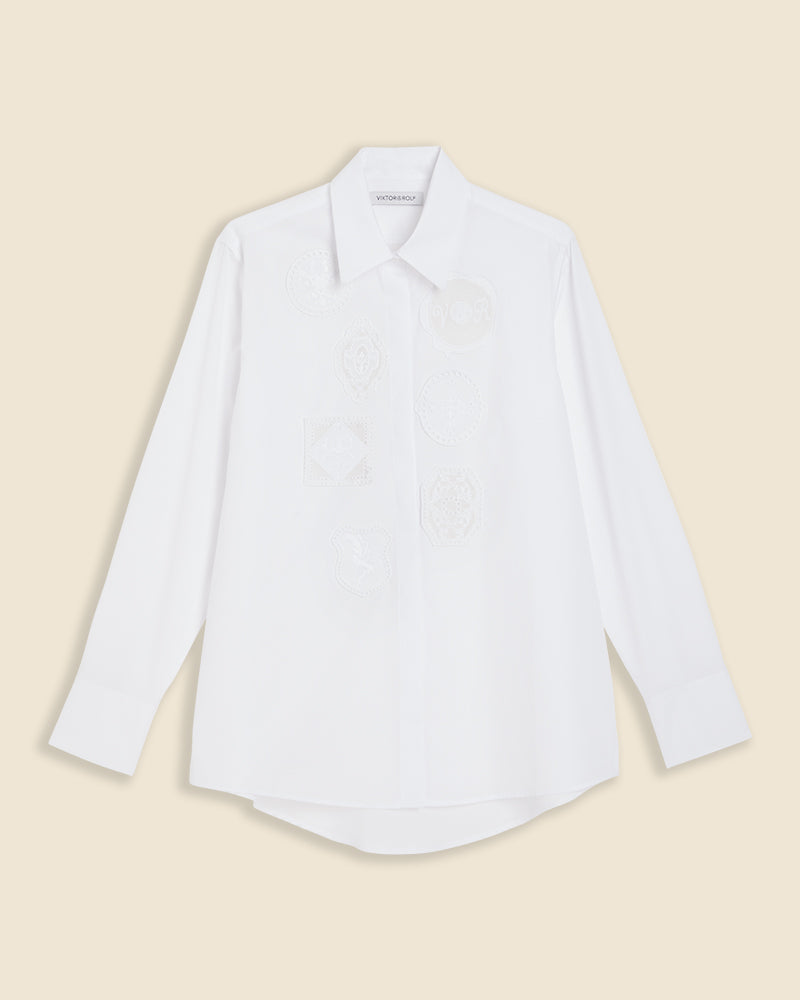 White long-sleeved shirt featuring subtle embroidered patterns on the front, with a classic collar and buttoned cuffs.