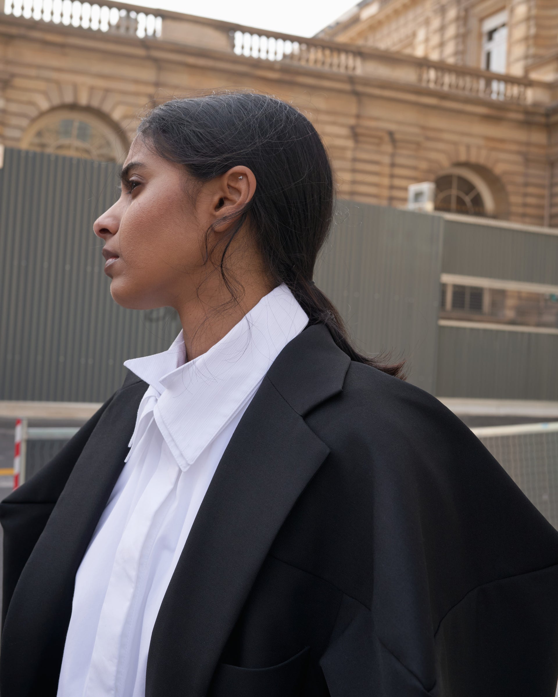 Person wearing a black blazer over a white shirt with a blurred background