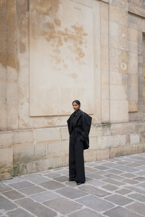 Person wearing a black outfit standing against a stone wall.