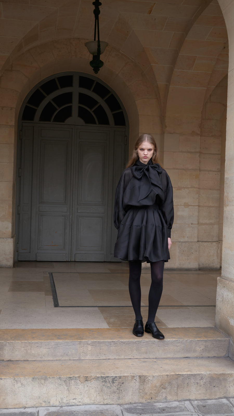 Woman standing outside of a building wearing a black mini dress.