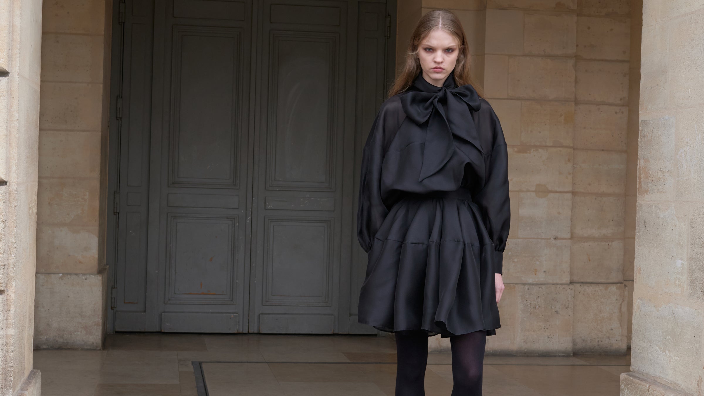 Woman standing outside of a building wearing a black mini dress.