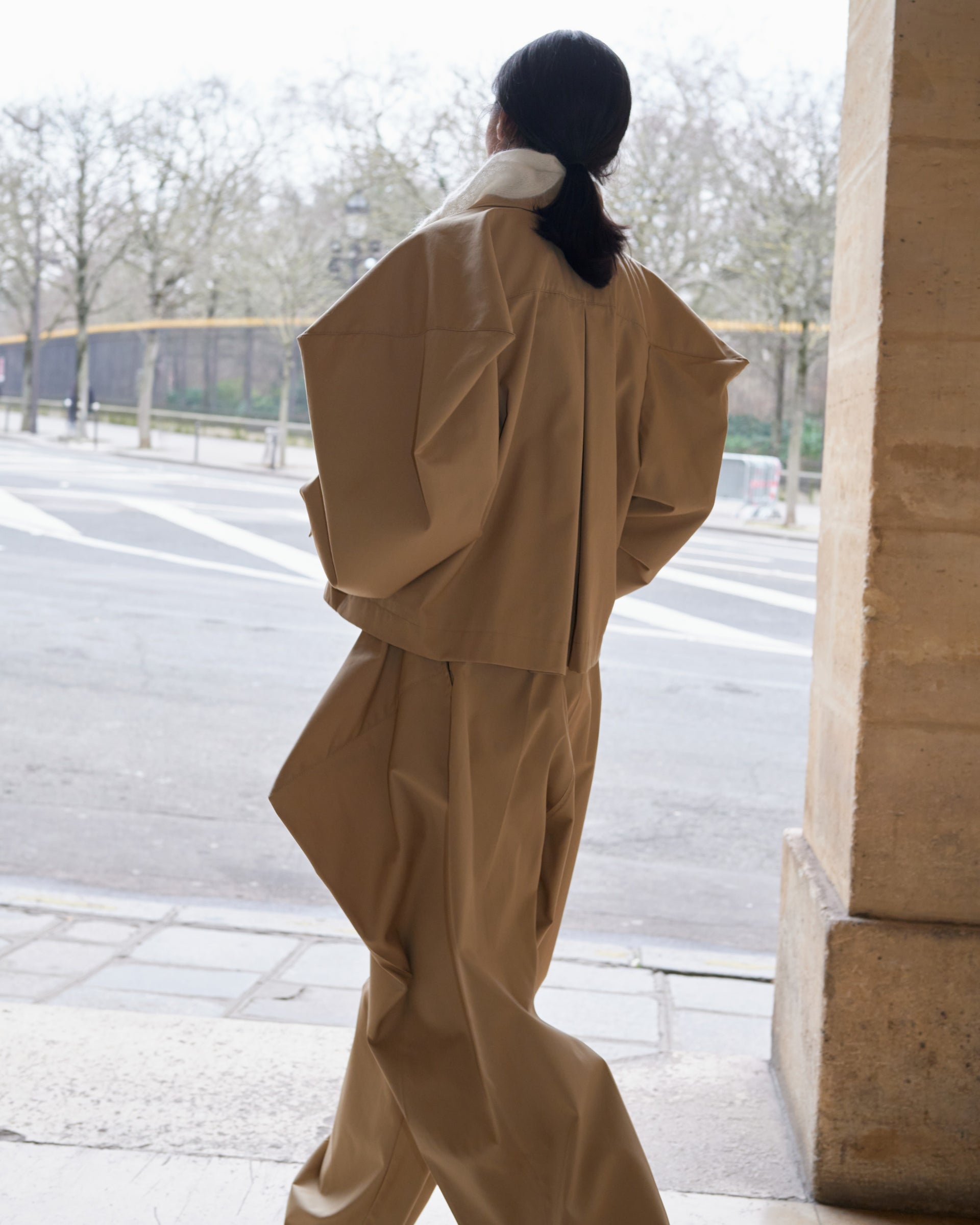 Person wearing a beige trench coat walking away from a building entrance.
