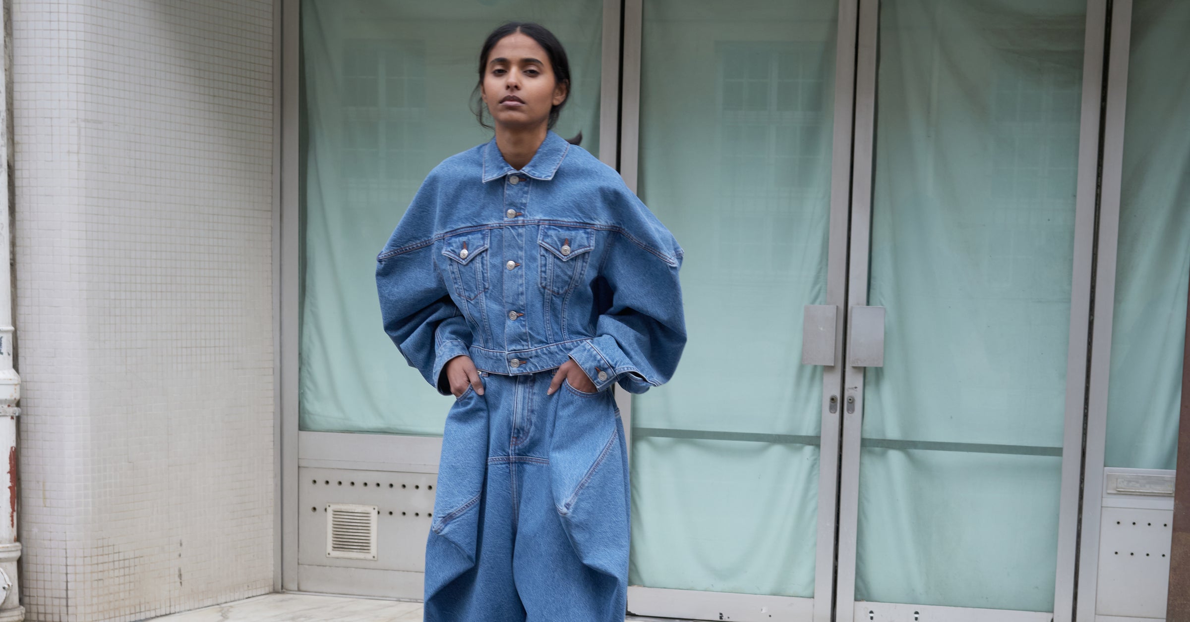 Person wearing a blue denim outfit standing in front of a glass door.