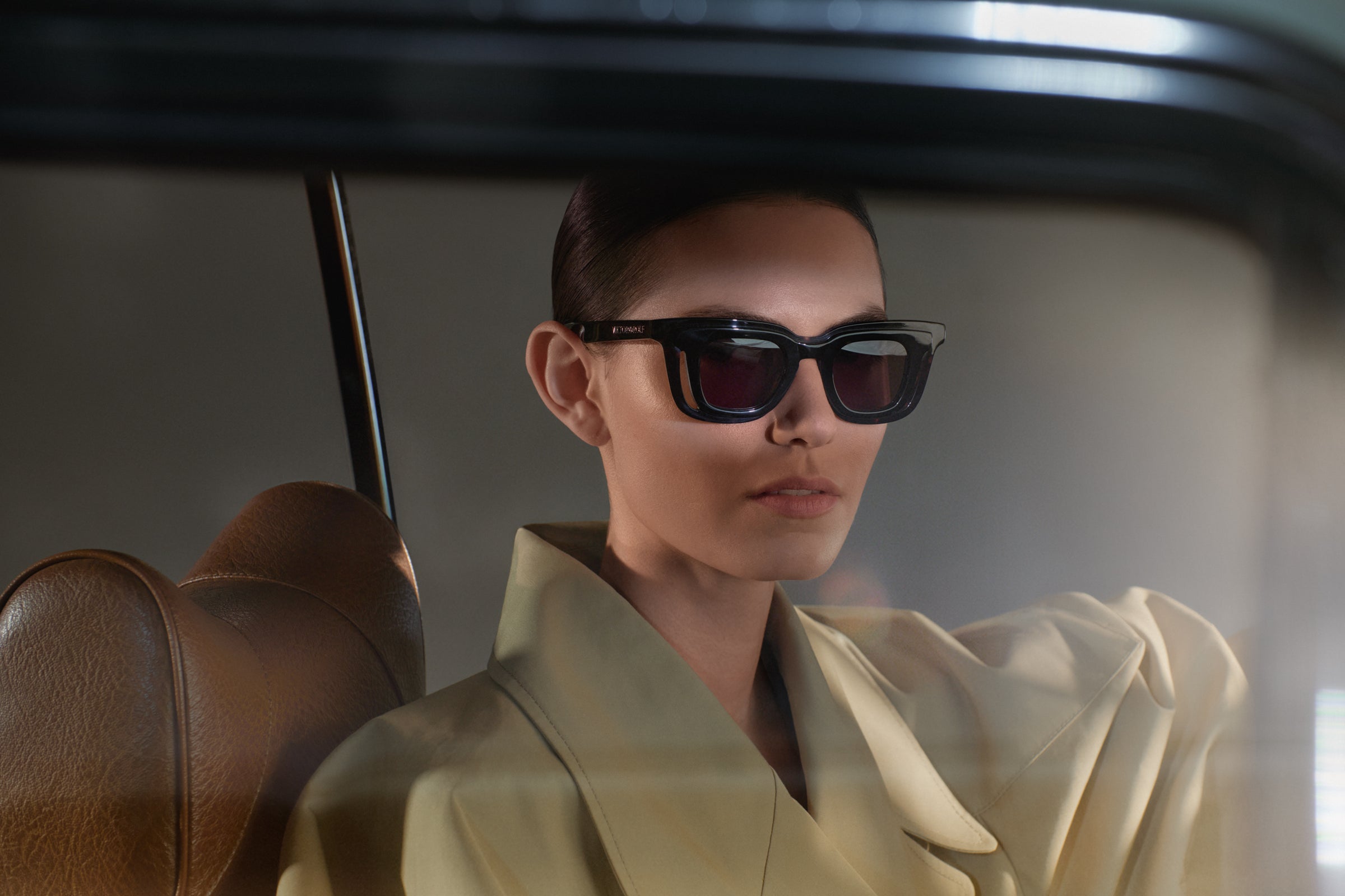 Person wearing sunglasses and a light-colored outfit inside a vehicle.