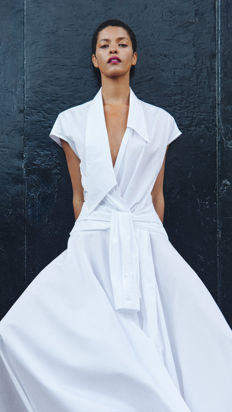Woman wearing a white sleeveless dress against a dark textured wall