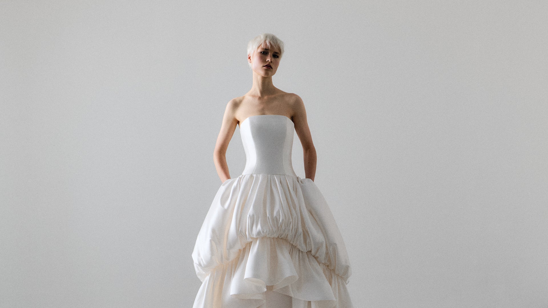 Woman wearing a white strapless gown with a layered skirt against a plain background