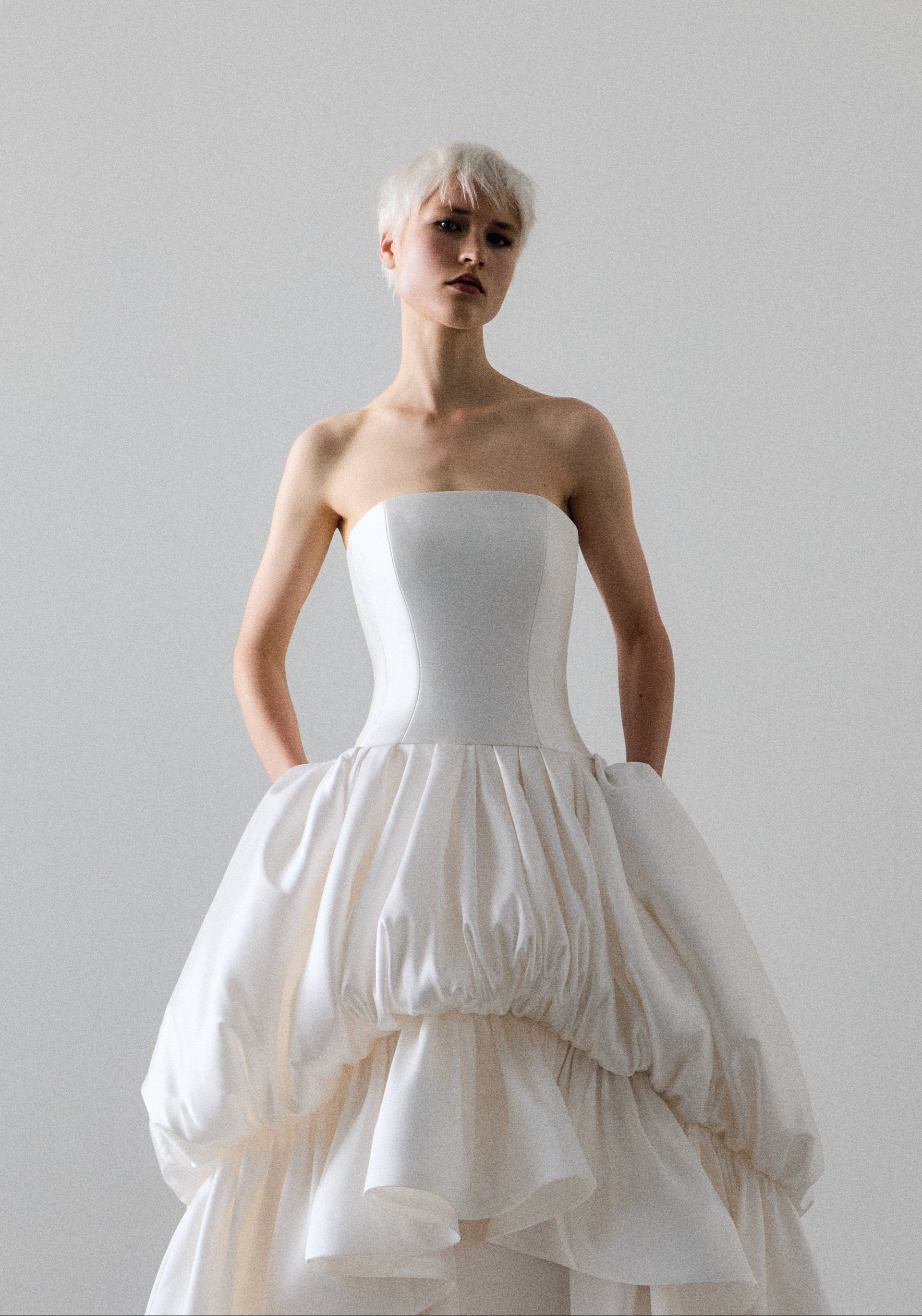 Woman wearing a white strapless gown with a layered skirt against a plain background