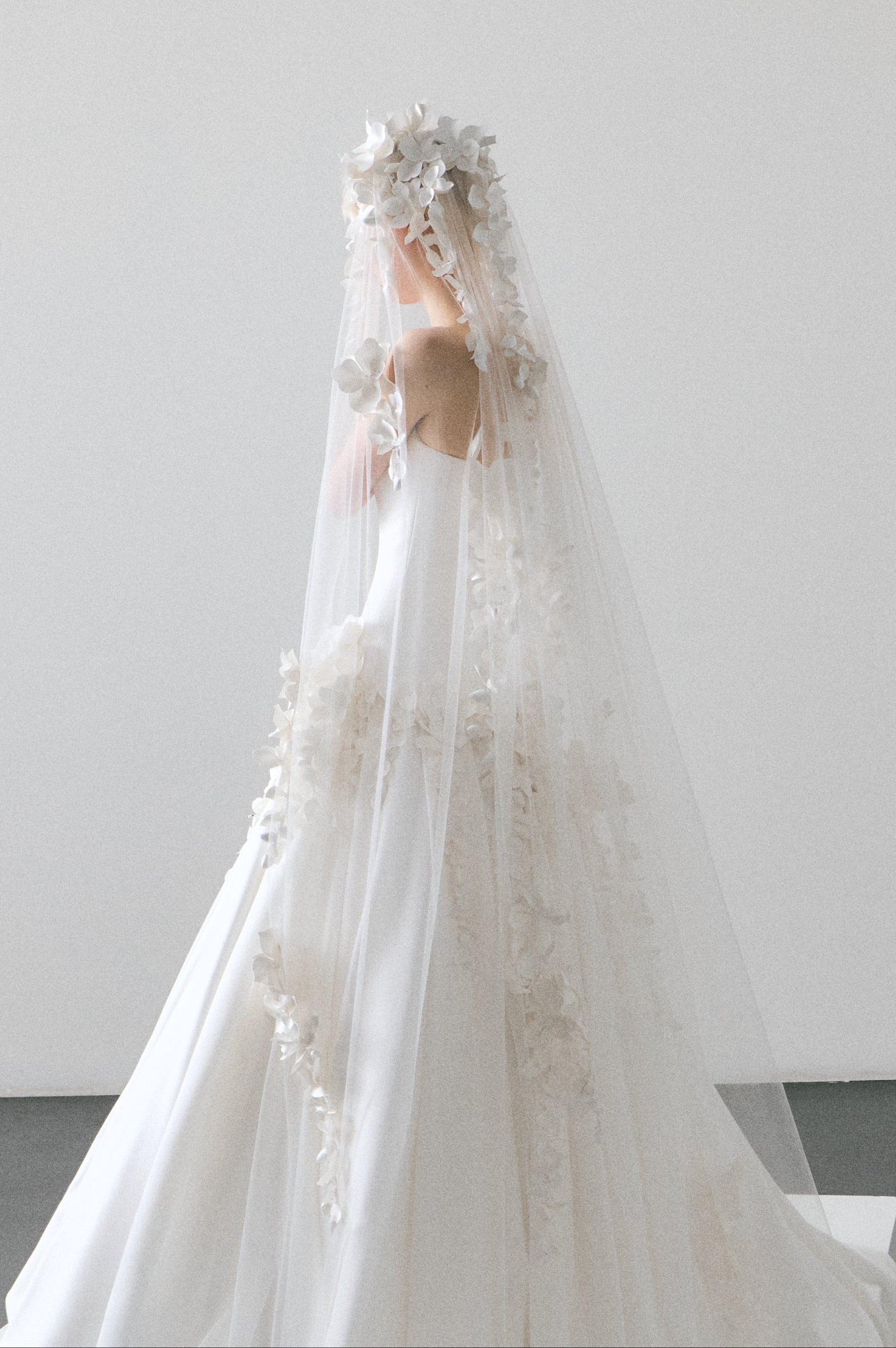 White wedding dress with a long veil on a plain background